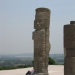 A man standing next to two large stone statues.