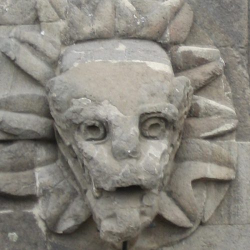 A stone face with a sun on it's forehead.