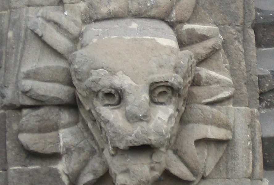 A stone face with a sun on it's forehead.