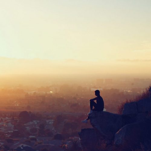 A man sitting on top of a mountain looking at the sunset.