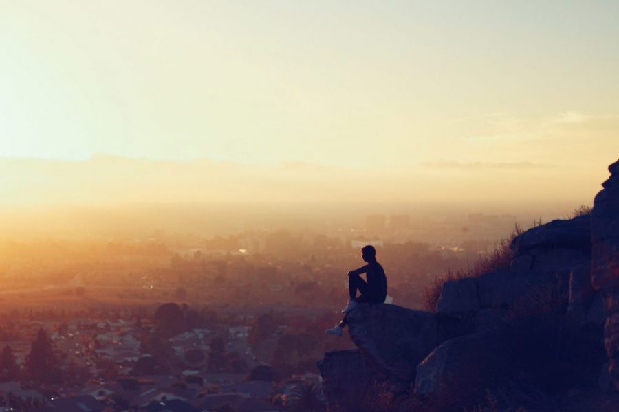 A man sitting on top of a mountain looking at the sunset.
