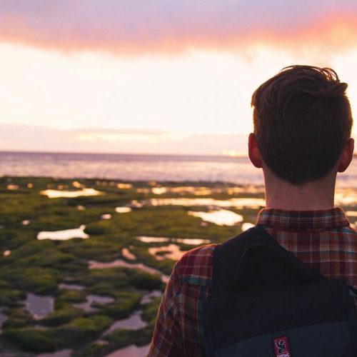 A man standing on top of a beach looking at the water.