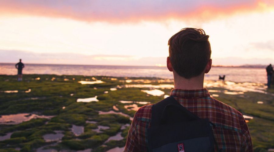 A man standing on top of a beach looking at the water.