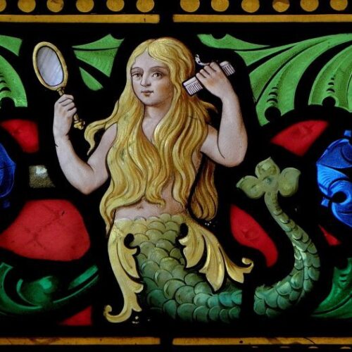 A stained glass window of a mermaid with a mirror and brush.