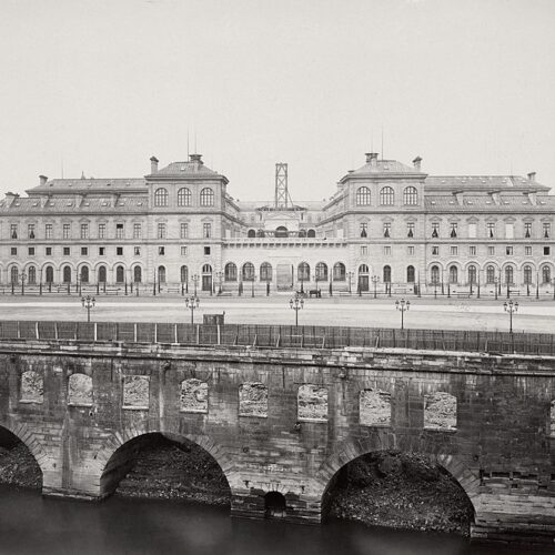 Historic stone bridge over a river with a grand building in the background.