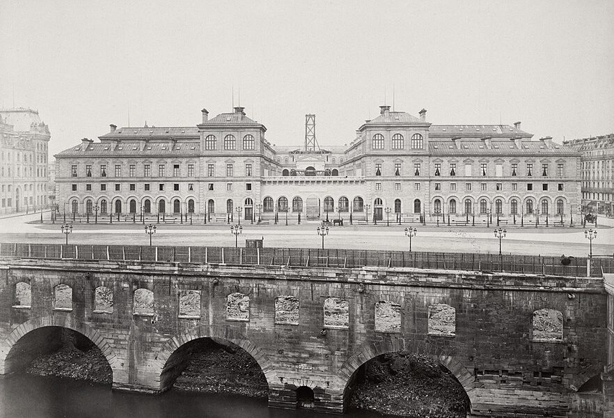 Historic stone bridge over a river with a grand building in the background.
